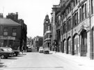 View: s18349 Norfolk Street from junction with Change Alley, Nos. 26 - 38 premises belonging to Thomas A. Ashton Ltd., right, Nos. 43 - 45 Harry Hartley and Son Ltd., hardware stores, left, Victoria Hall and St. Marie's RC Church in background