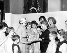 Mrs. Thorpe, wife of chairman of Libraries, Art Galleries and Museums Committee with John Pilley holding award for best decorated Childrens Library, Firth Park Branch Library, Christmas 1958