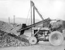 Fordson tractor with primitive bulldozer on front, slag (or crushed rock) used for road repairs