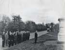 First World War reunion visit (to Ypres, Belgium?) featuring group of veterans lined up along a roadside in front of a war memorial, [c. 1930s?]
